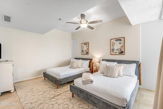 bedroom featuring ceiling fan, light tile patterned floors, and a textured ceiling