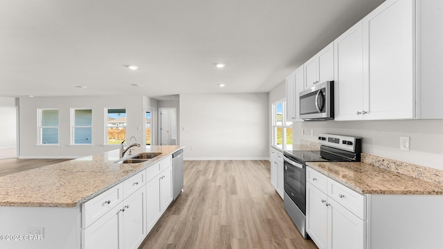 kitchen with sink, light stone countertops, light wood-type flooring, white cabinetry, and stainless steel appliances