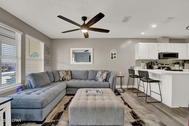 living room featuring light hardwood / wood-style floors, a textured ceiling, and ceiling fan