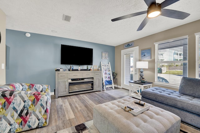 living room featuring ceiling fan, a textured ceiling, light wood-type flooring, and a fireplace