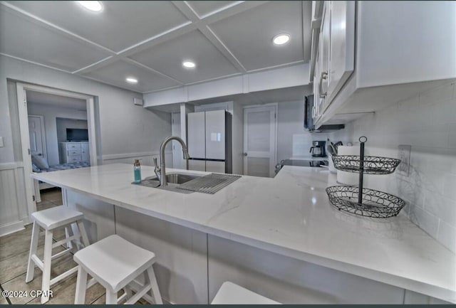 kitchen with kitchen peninsula, light stone counters, sink, white refrigerator, and a breakfast bar area