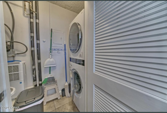 laundry area with a textured ceiling, stacked washing maching and dryer, and light tile patterned flooring