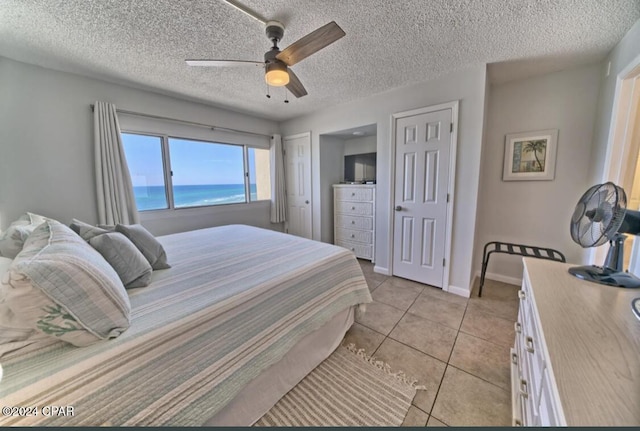 bedroom featuring ceiling fan, light tile patterned floors, and a textured ceiling