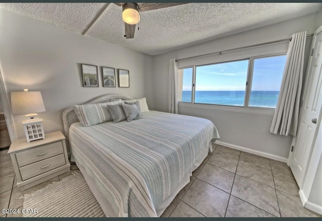 tiled bedroom featuring ceiling fan, a water view, and a textured ceiling