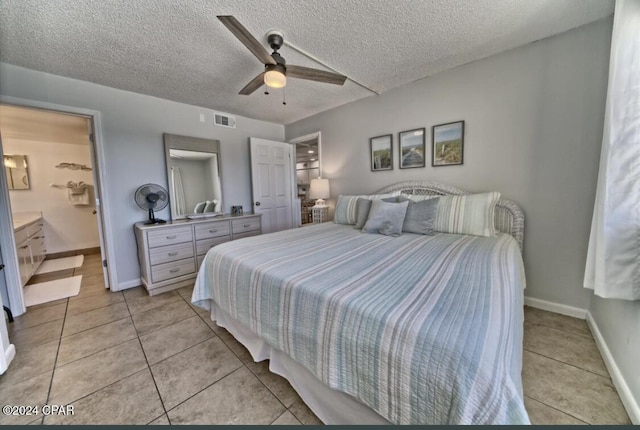 bedroom featuring ceiling fan, light tile patterned floors, a textured ceiling, and ensuite bath