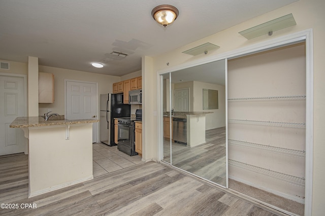 kitchen featuring visible vents, light wood-type flooring, appliances with stainless steel finishes, a peninsula, and a breakfast bar area