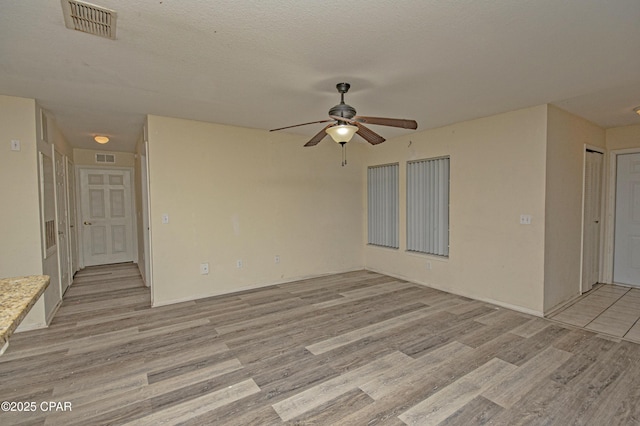 empty room featuring visible vents, ceiling fan, a textured ceiling, and light wood-style flooring