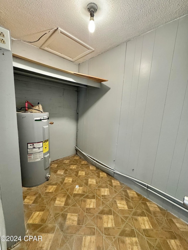 interior space with electric water heater, a textured ceiling, and wooden walls