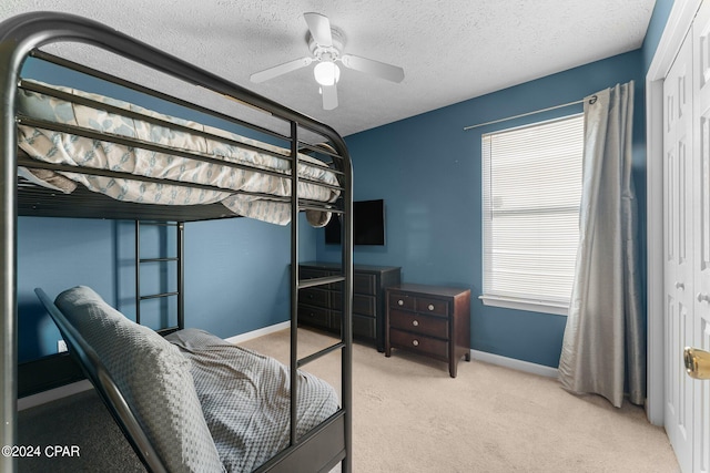 bedroom with ceiling fan, a closet, light colored carpet, and a textured ceiling