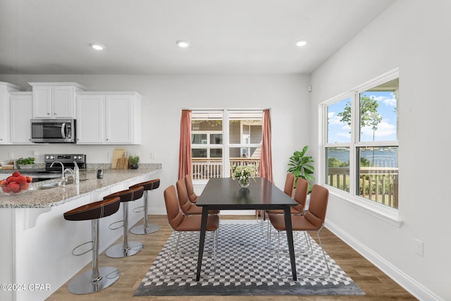 kitchen with appliances with stainless steel finishes, white cabinetry, light stone countertops, a kitchen bar, and dark hardwood / wood-style floors