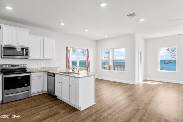 kitchen with appliances with stainless steel finishes, sink, dark hardwood / wood-style flooring, white cabinets, and a water view