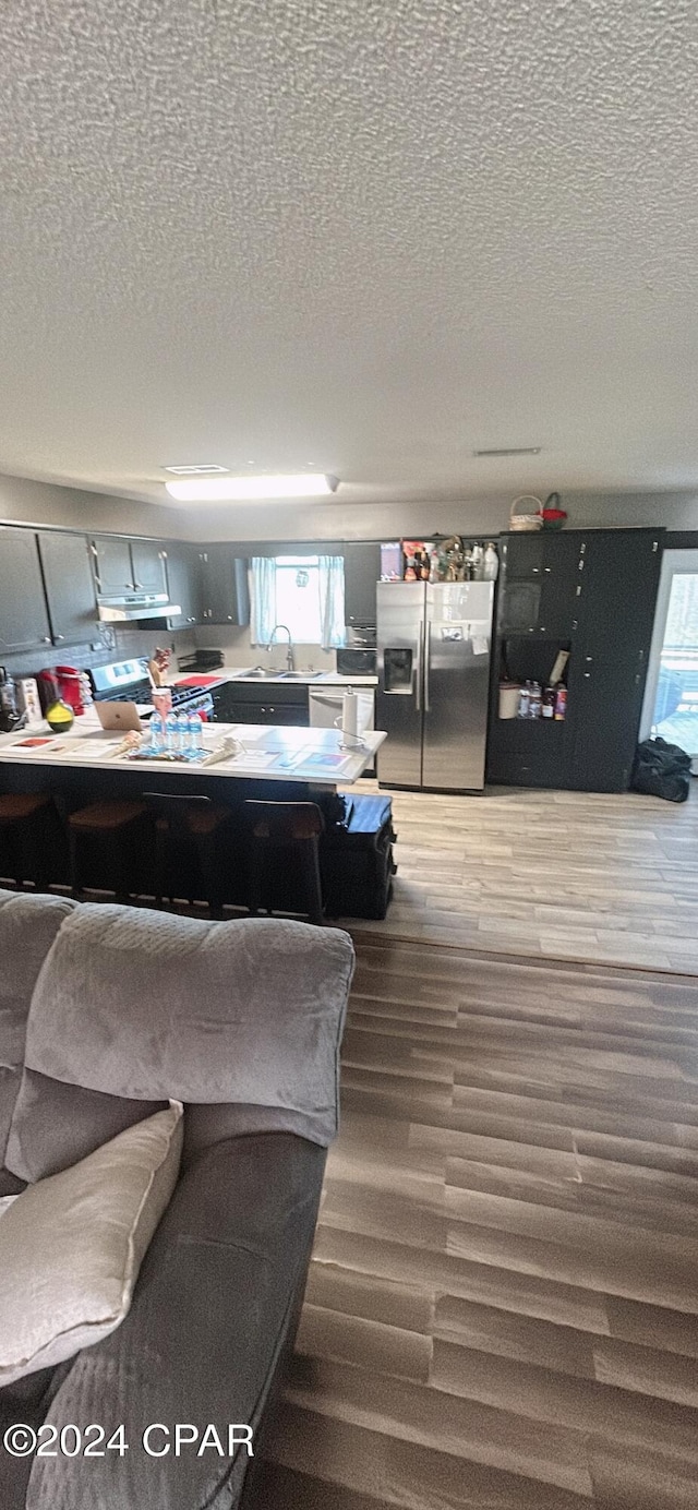 interior space featuring stainless steel refrigerator with ice dispenser, a textured ceiling, hardwood / wood-style flooring, and sink