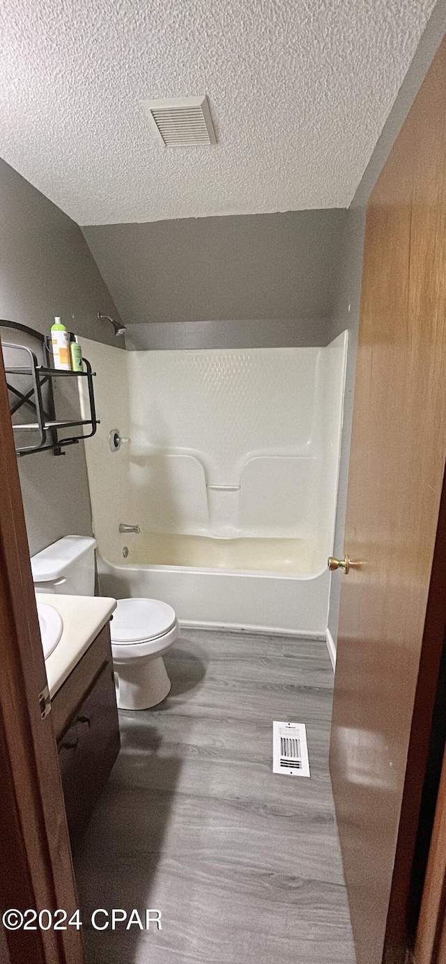 full bathroom with hardwood / wood-style floors, vanity, shower / washtub combination, vaulted ceiling, and a textured ceiling