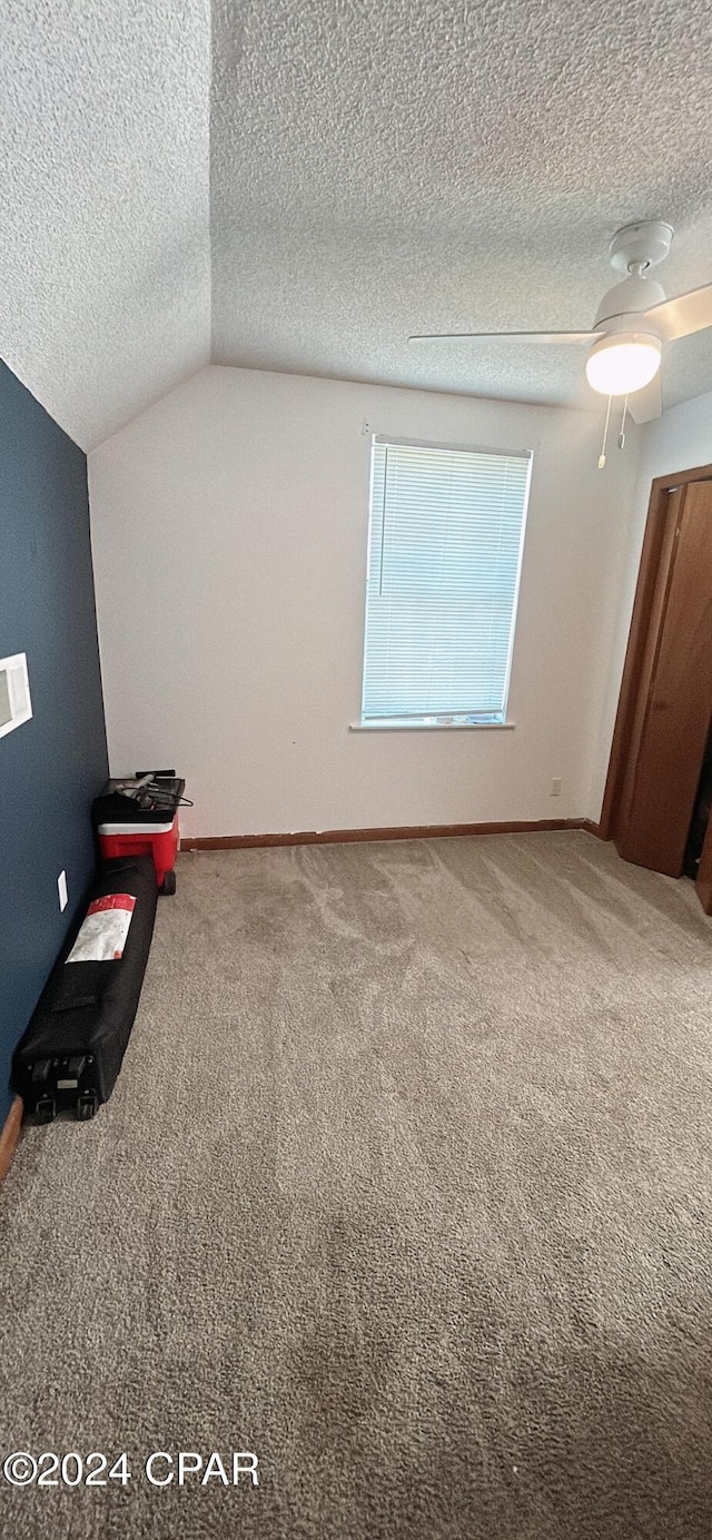 unfurnished bedroom featuring a textured ceiling, ceiling fan, carpet floors, and vaulted ceiling