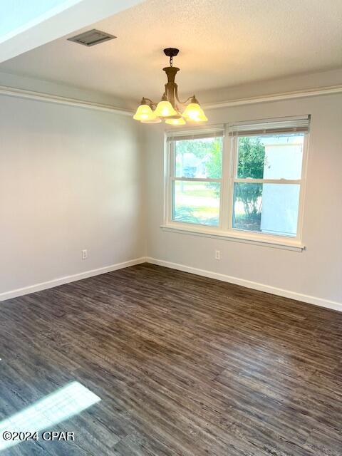 spare room with baseboards, visible vents, ornamental molding, dark wood-style flooring, and a chandelier