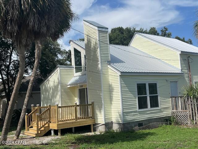 rear view of house featuring metal roof, crawl space, a wooden deck, and a lawn