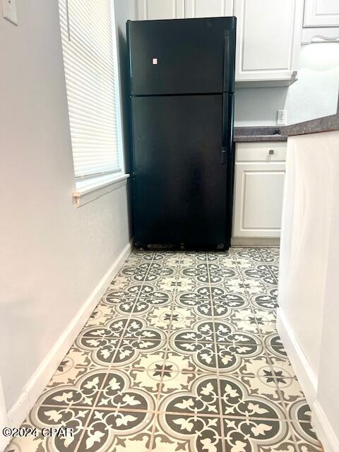 kitchen with baseboards, dark countertops, freestanding refrigerator, and white cabinetry