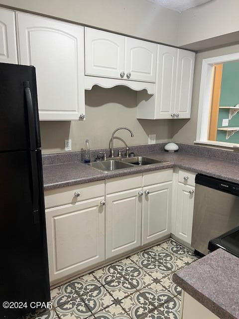 kitchen featuring stainless steel dishwasher, a sink, freestanding refrigerator, and white cabinetry