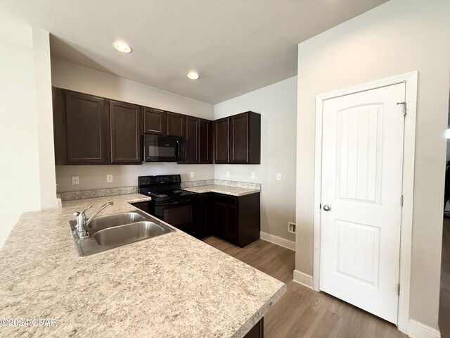 kitchen featuring dark brown cabinetry, sink, kitchen peninsula, light hardwood / wood-style floors, and black appliances