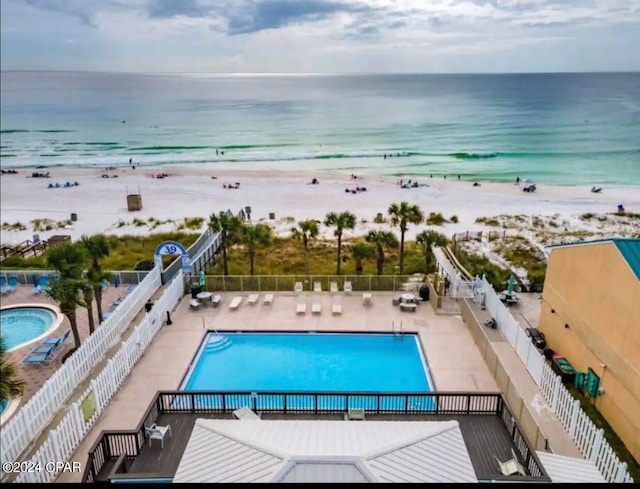 view of swimming pool featuring a patio area, a water view, and a view of the beach