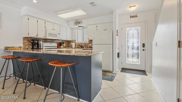 kitchen featuring white appliances, light stone counters, kitchen peninsula, light tile patterned floors, and white cabinetry