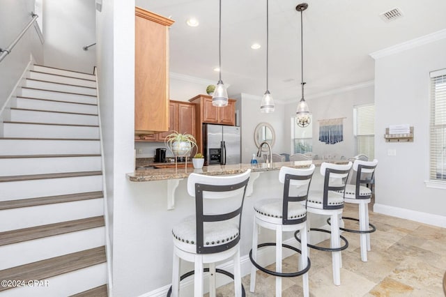 kitchen featuring light stone counters, decorative light fixtures, stainless steel refrigerator with ice dispenser, crown molding, and a kitchen bar