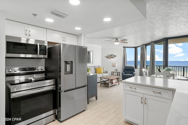 kitchen featuring a textured ceiling, ceiling fan, stainless steel appliances, white cabinets, and a water view