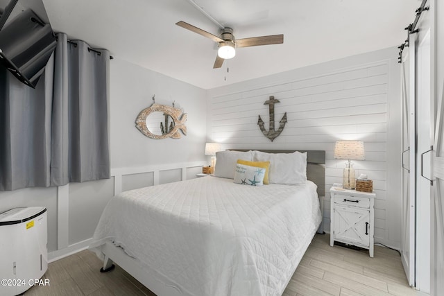 bedroom with a barn door, light wood-type flooring, and ceiling fan