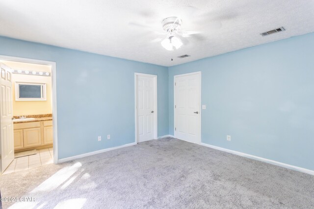 unfurnished bedroom featuring ensuite bath, light carpet, a textured ceiling, and ceiling fan