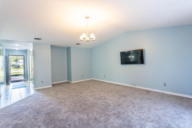 carpeted empty room with lofted ceiling and a chandelier