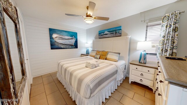 bedroom with wooden walls, light tile patterned floors, and ceiling fan