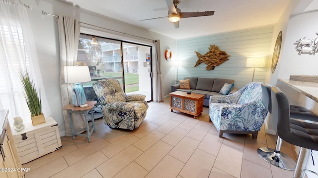 living room with a ceiling fan, an accent wall, wood walls, and light tile patterned floors