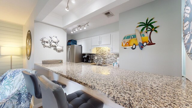 kitchen with kitchen peninsula, light stone countertops, white cabinetry, stainless steel refrigerator, and tasteful backsplash