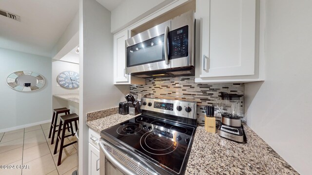 kitchen featuring appliances with stainless steel finishes, light stone counters, white cabinetry, and light tile patterned floors