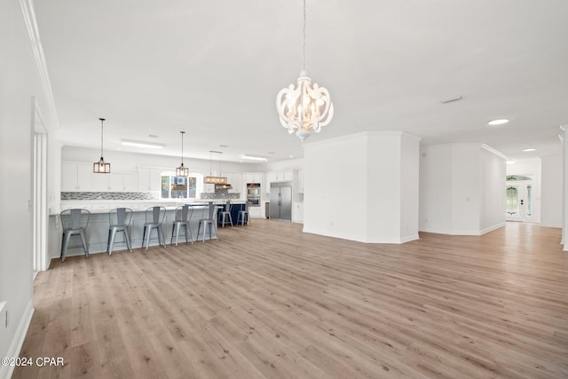 unfurnished living room with an inviting chandelier, crown molding, and light hardwood / wood-style flooring