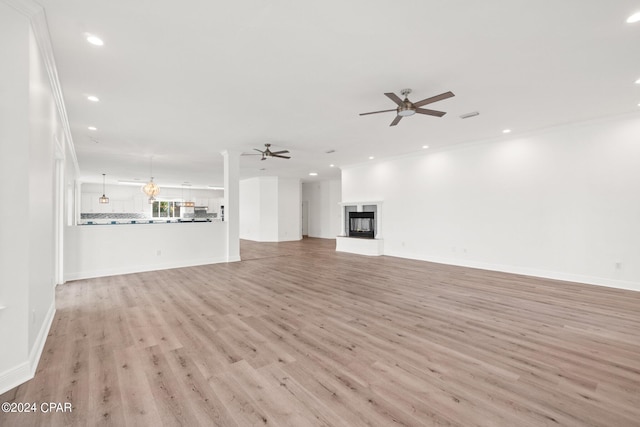 unfurnished living room with a multi sided fireplace, crown molding, and light wood-type flooring