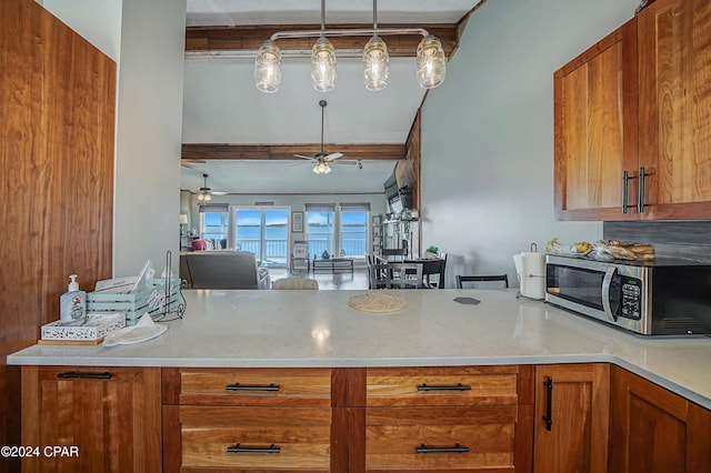 kitchen with brown cabinetry, a ceiling fan, stainless steel microwave, open floor plan, and light stone countertops