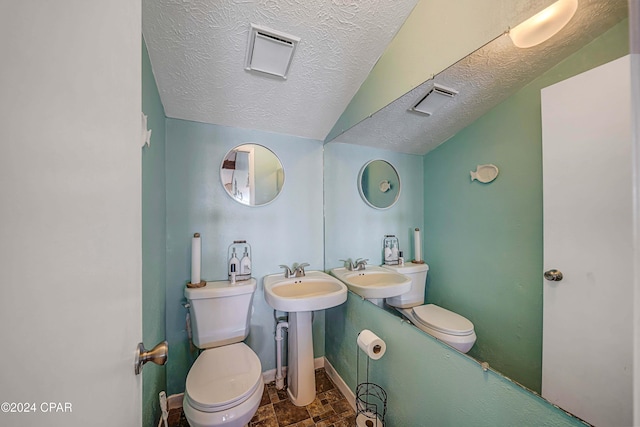 half bathroom with toilet, vaulted ceiling, a sink, a textured ceiling, and baseboards