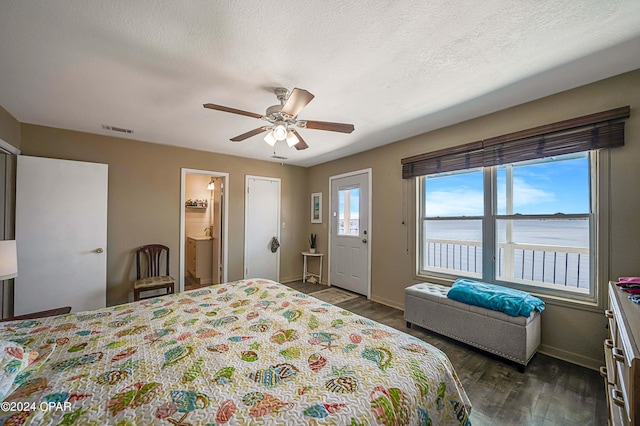 bedroom with a water view, visible vents, dark wood-type flooring, a textured ceiling, and baseboards