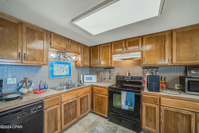 kitchen with brown cabinetry, a sink, under cabinet range hood, and black appliances