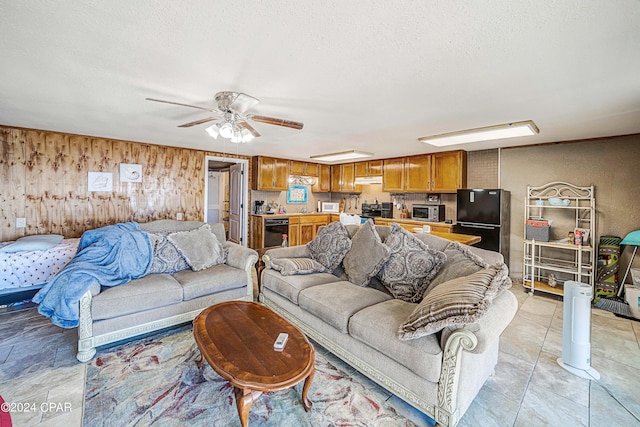 living room with ceiling fan, a textured ceiling, and wooden walls