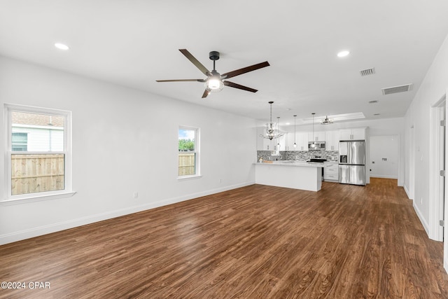 unfurnished living room with ceiling fan with notable chandelier, plenty of natural light, and dark hardwood / wood-style flooring