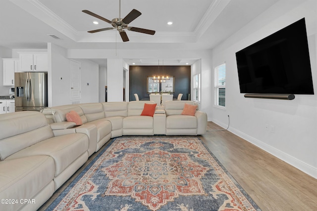 living room featuring crown molding, ceiling fan with notable chandelier, light hardwood / wood-style floors, and a raised ceiling