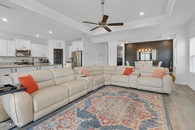 living room with ornamental molding, ceiling fan with notable chandelier, light hardwood / wood-style flooring, and a raised ceiling