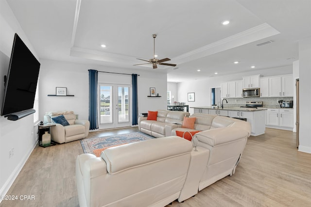 living room featuring light wood-type flooring, ceiling fan, and a raised ceiling