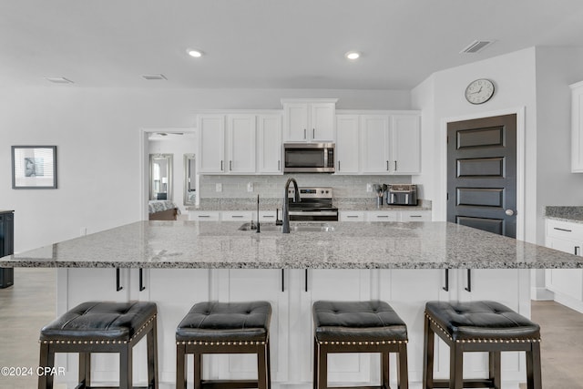 kitchen with white cabinetry, appliances with stainless steel finishes, a kitchen bar, a large island with sink, and decorative backsplash