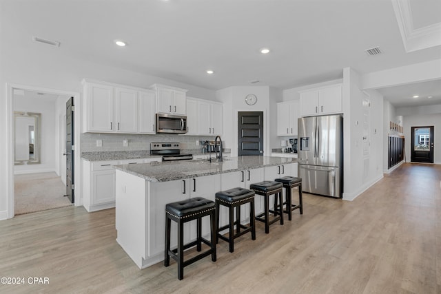 kitchen with light hardwood / wood-style floors, white cabinetry, a kitchen island with sink, and appliances with stainless steel finishes