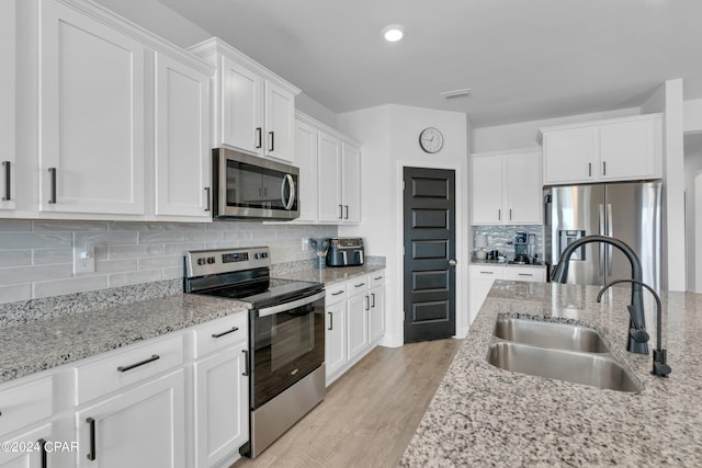 kitchen featuring sink, light stone counters, appliances with stainless steel finishes, light hardwood / wood-style flooring, and white cabinets