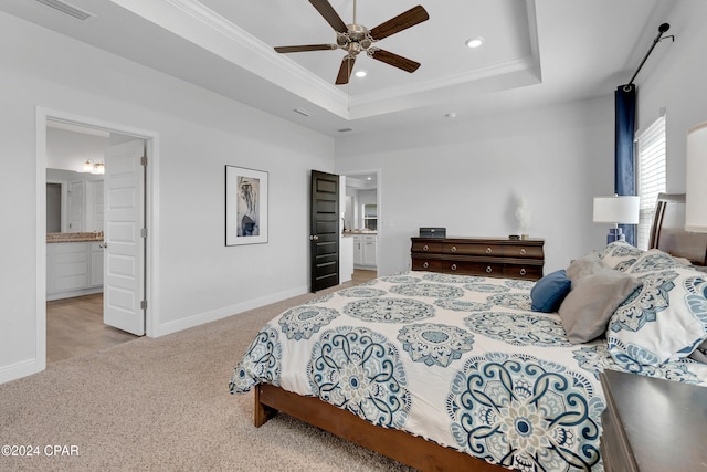 carpeted bedroom with ensuite bathroom, ceiling fan, crown molding, and a tray ceiling