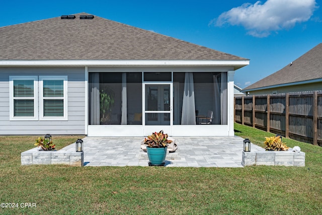 rear view of property featuring a patio, a sunroom, and a lawn